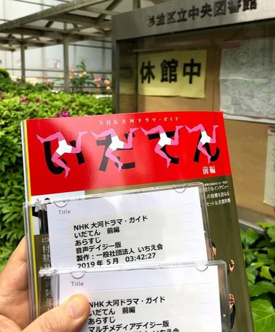 いだてんムック本、音声デイジー版CD、マルチメディアデイジー版CD(休館中の表示がある杉並区立中央図書館前にて)